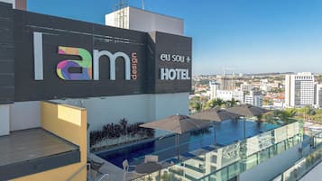 Letrero de hotel con la marca 'lam' y 'eu sou +', piscina en la azotea con sillas de descanso y vistas a la ciudad.