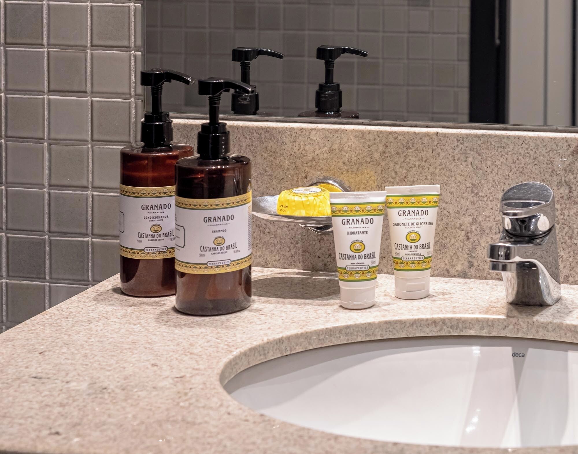 A bathroom counter with toiletries including two bottles of Castanha do Brasil conditioner, a yellow bar of soap, and two tubes of Castanha do Brasil hydrating lotion.