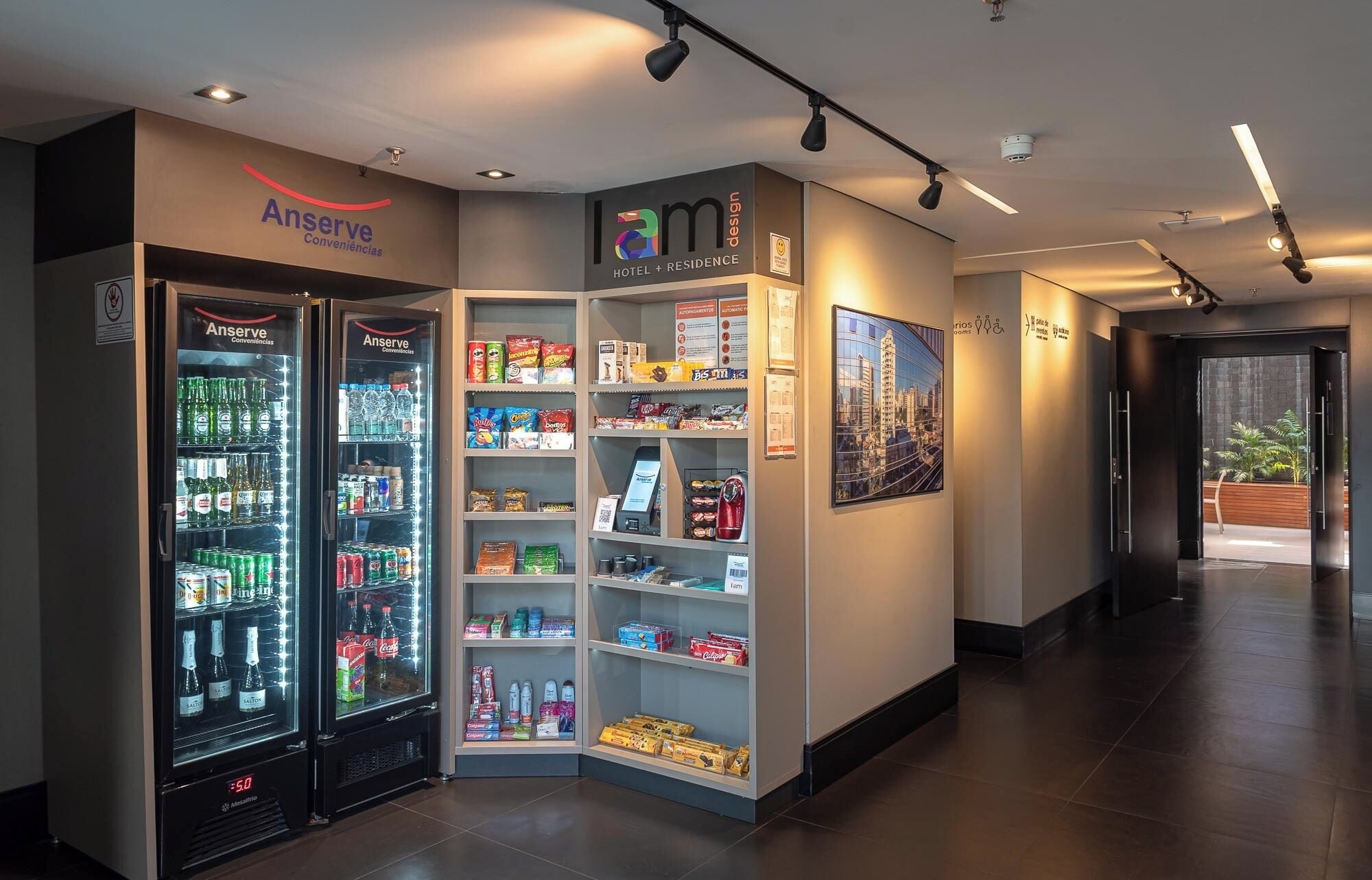 Un hall d'hôtel équipé d'un distributeur automatique de boissons en libre-service, d'une enseigne au « design lam » et d'une affiche décorative accrochée au mur.
