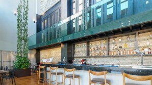 Zona de bar moderna con techo alto, taburetes de madera y una variedad de botellas de licor.