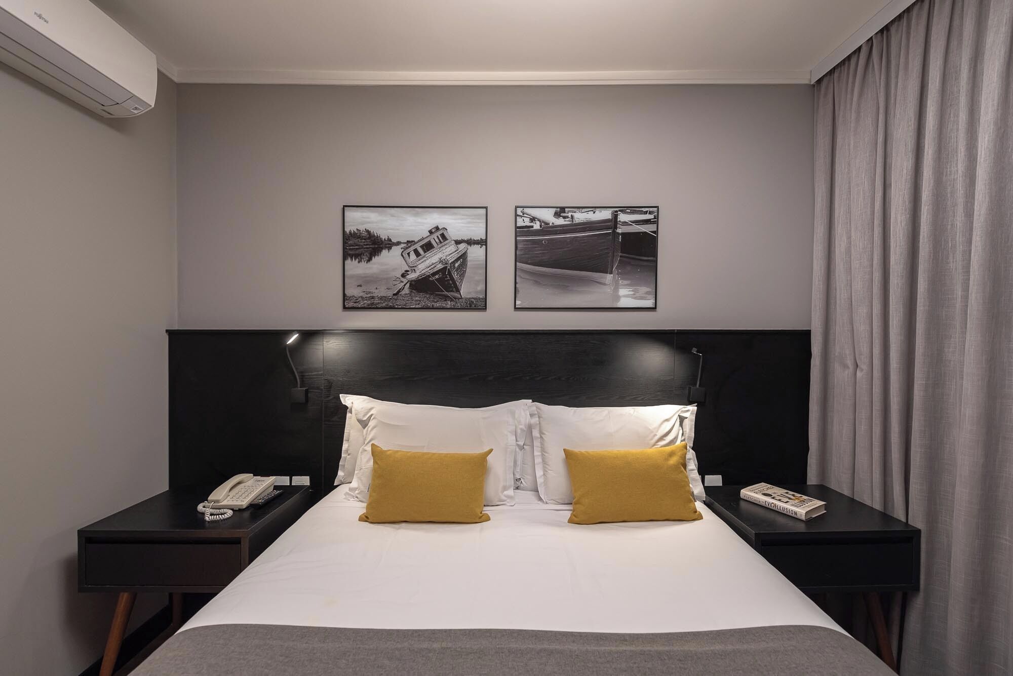 A hotel room with a large bed, two nightstands, a black headboard, and two framed pictures on the wall.