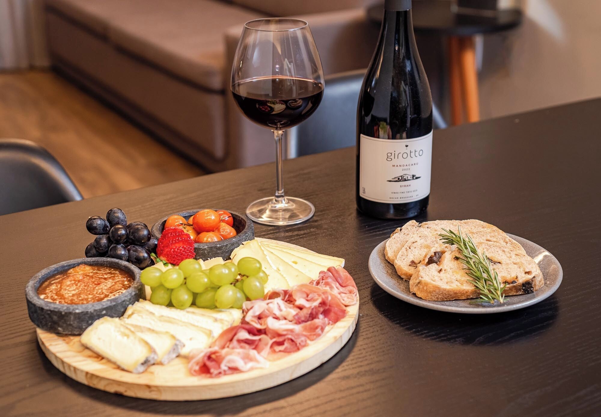 A charcuterie board with cheese, meats, fruits, and a bottle of wine on a table.