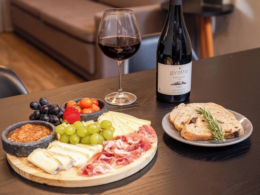 Una tabla de embutidos con queso, carnes, frutas y una botella de vino sobre una mesa.