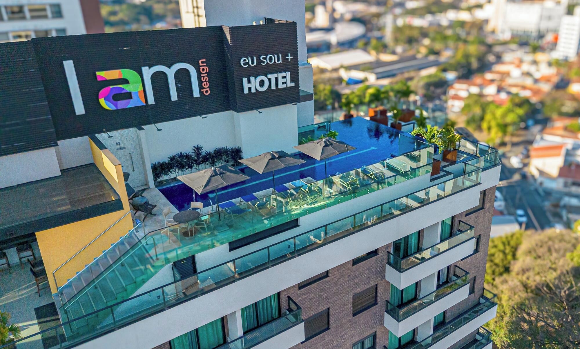 A modern hotel with a rooftop pool area, glass railings, and outdoor seating.