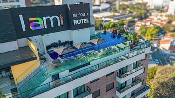 A modern hotel with a rooftop pool area, glass railings, and outdoor seating.