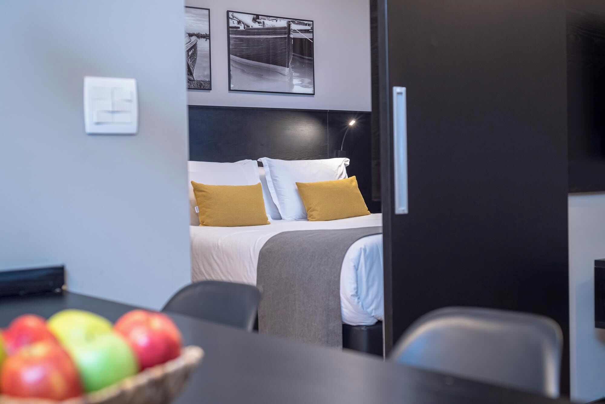 Hotellihuoneessa on sänky, yöpöytä, jossa on kulho täynnä omenoita, ja tuoli. Sängyn yläpuolella seinällä on kaksi kehystettyä kuvaa.