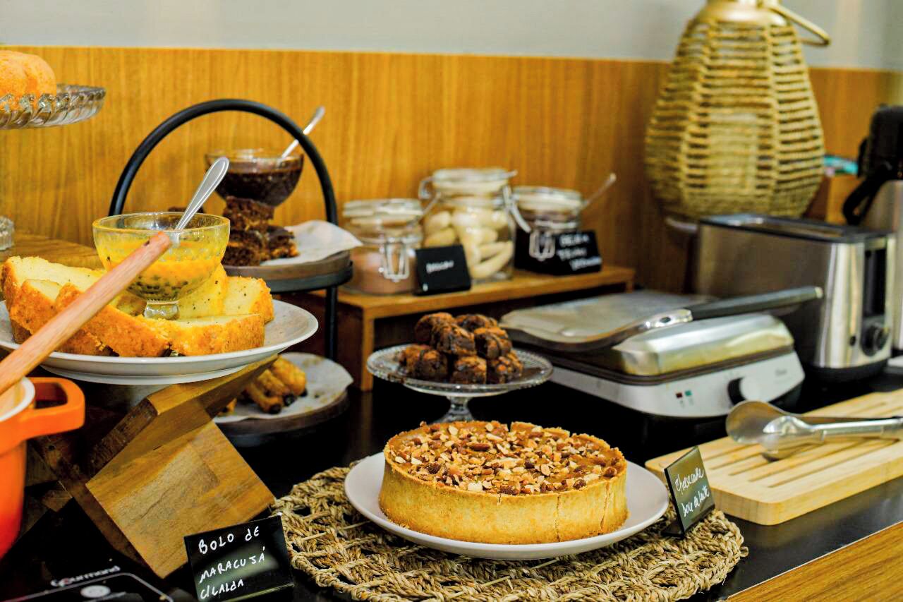 Buffet com diversos alimentos, incluindo bolo, pão e potes com patês.