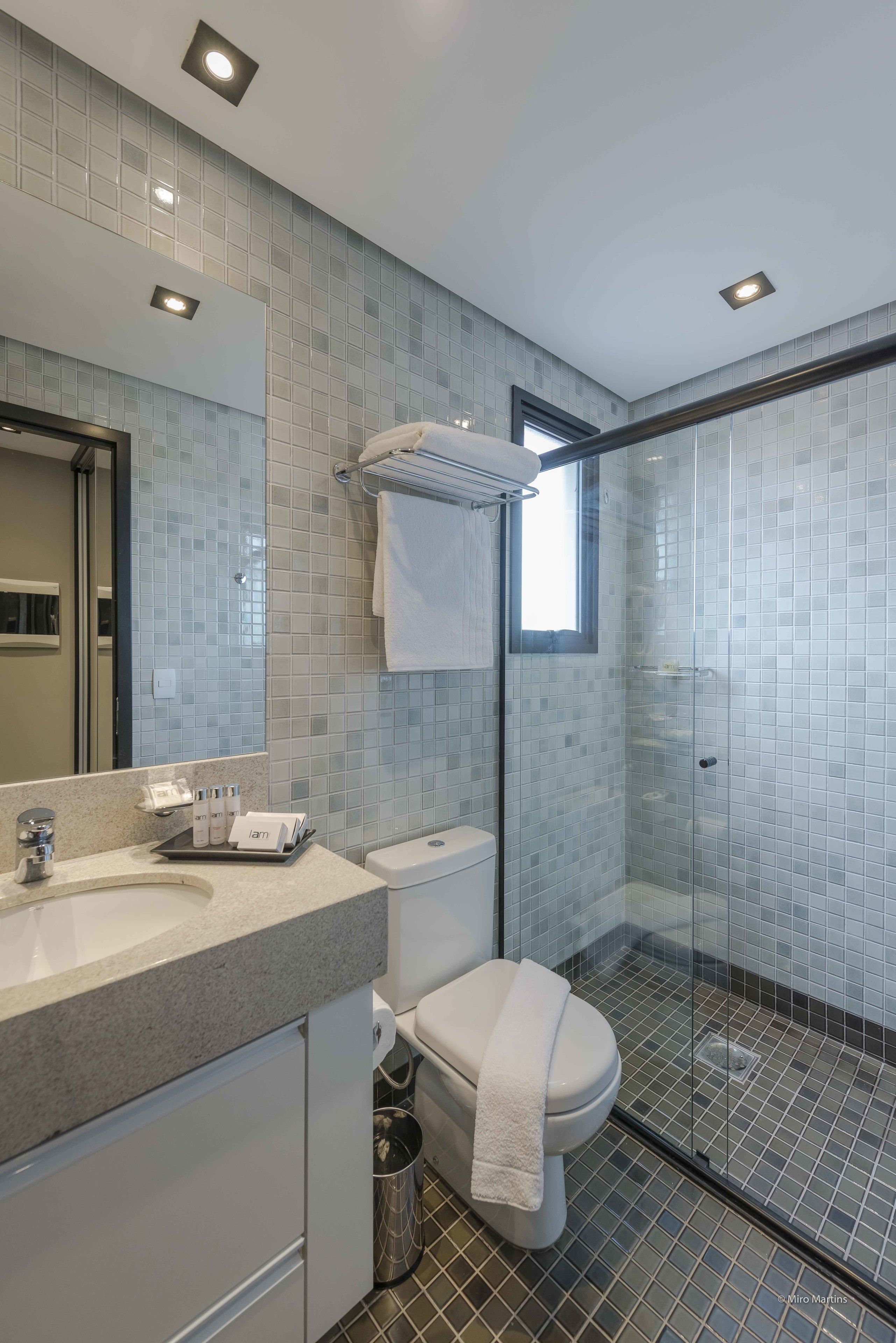 A modern bathroom with a glass-enclosed shower, a large mirror, and a vanity with a sink and toiletries.