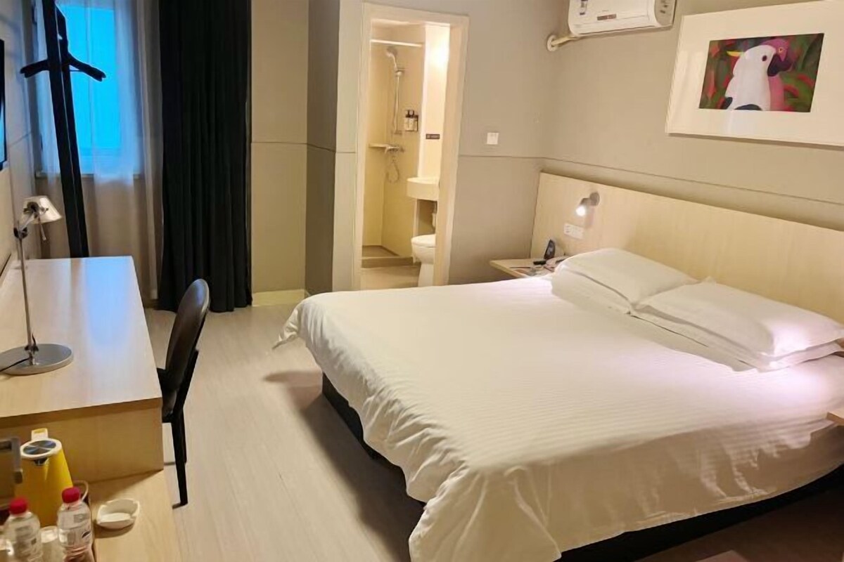 Habitación de hotel con cama, escritorio, silla y baño visible a través de una puerta abierta.