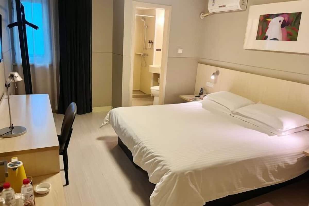 Une chambre d’hôtel avec un lit, un bureau, une chaise et une salle de bain visible à travers une porte ouverte.