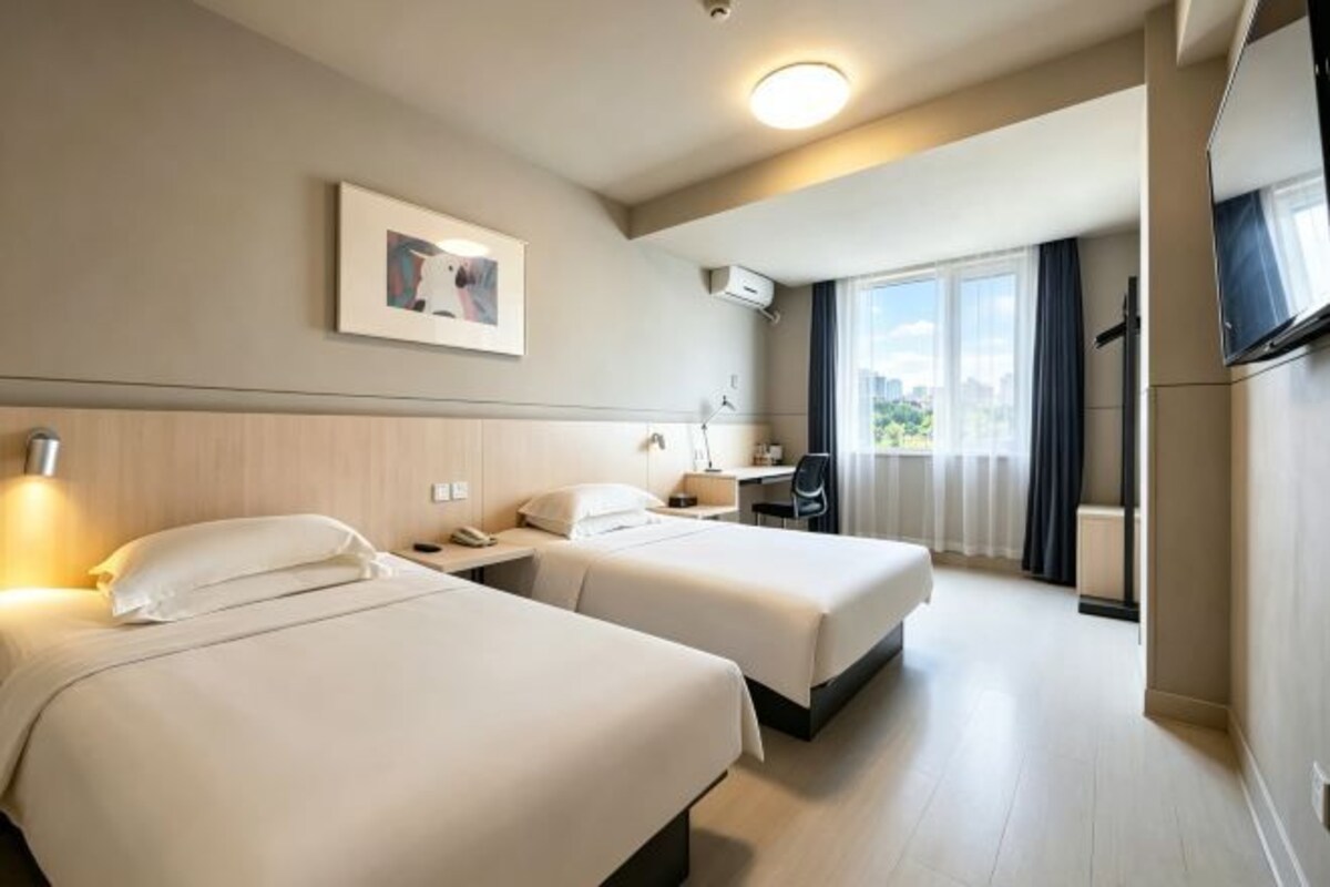 Habitación de hotel con dos camas, un escritorio, una silla, un televisor y una ventana con cortinas.