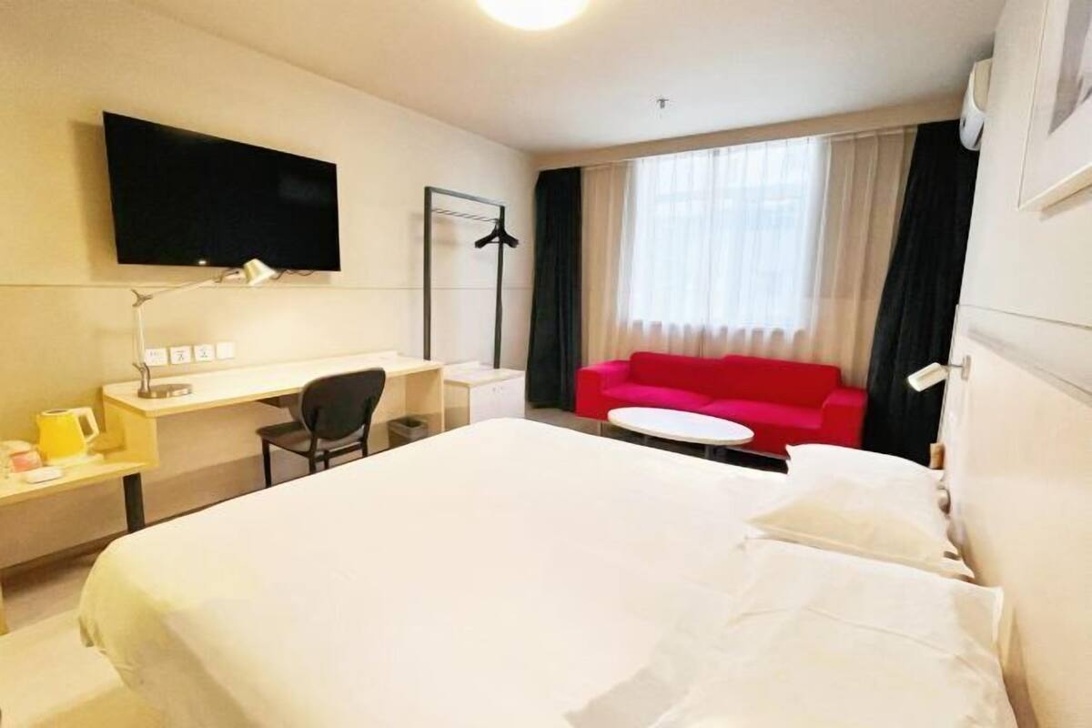 Hotellihuone, jossa on suuri sänky, työpöytä tuolilla, seinälle asennettu televisio, punainen sohva ja ikkuna, jossa on verhot.