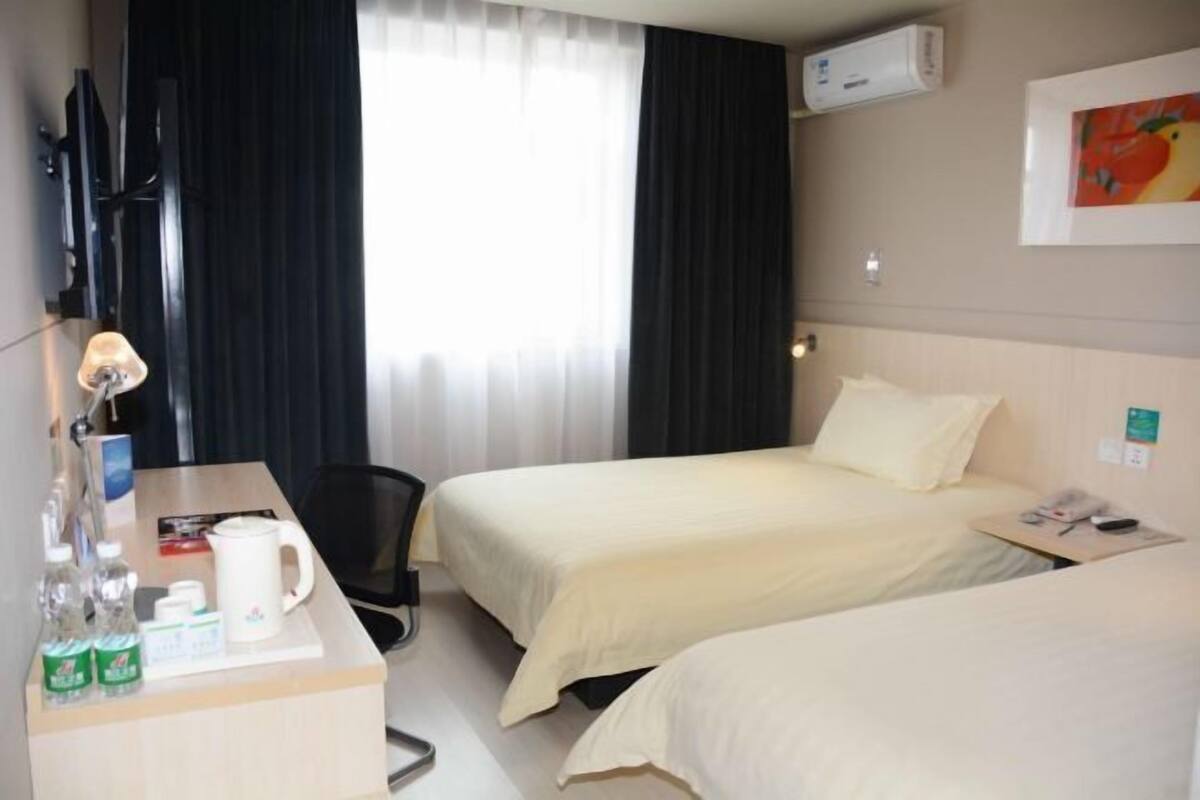 Hotellihuone, jossa on kaksi sänkyä, työpöytä lampun kanssa, televisio ja ikkuna, jossa on verhot.