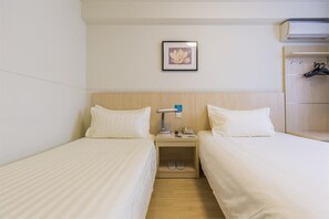 Habitación de hotel con dos camas individuales, una mesita de noche con lámpara, teléfono y un par de zapatillas.