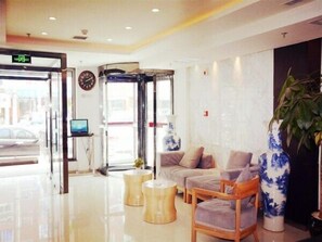 Un vestíbulo de hotel con una recepción, un sofá, un jarrón grande y una planta.