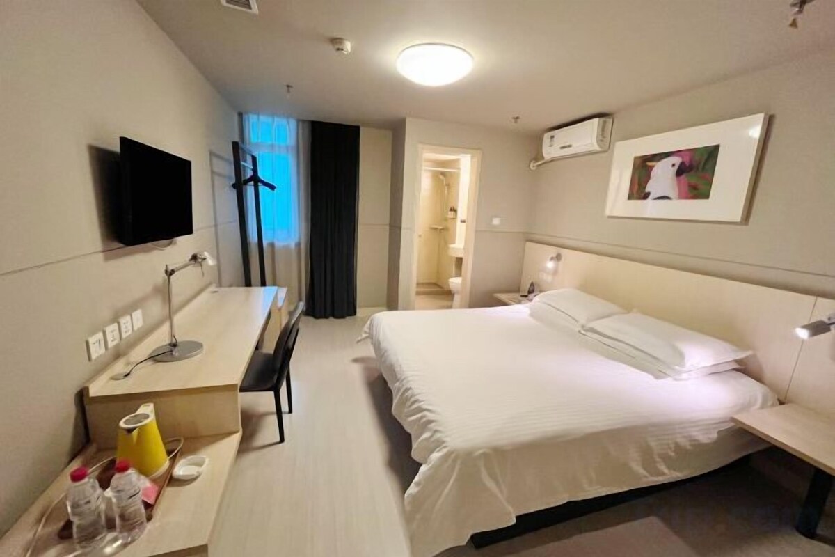 A hotel room with a bed, a desk, a chair, a television, and a bathroom visible through an open door.