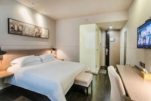 A hotel room with a bed, bedside table, bench, TV, and a door leading to a bathroom.