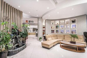Um hall moderno de hotel com um sofá modular, uma mesa de recepção e uma parede com quadros.