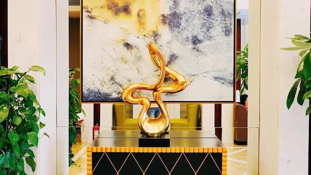 Een hal met een modern abstract schilderij, een gouden sculptuur en een zwart en oranje console.