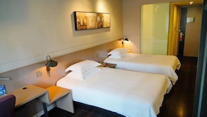 Hotelkamer met twee bedden, een bureau, een stoel, een wandlamp en een lijst met een afbeelding.