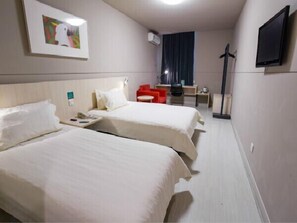 A hotel room with two beds, a desk, a chair, a TV, and a window with curtains.