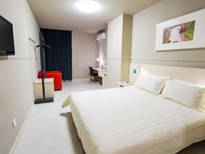 A hotel room with a large bed, a desk, a chair, and a TV mounted on the wall.