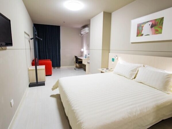 A hotel room with a large bed, a desk, a chair, and a TV mounted on the wall.