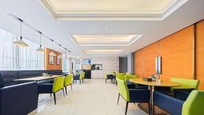 Un comedor moderno con cabinas y mesas redondas, una cocina al fondo e iluminación empotrada en el techo.
