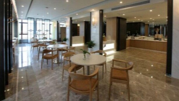 A modern hotel lobby with round tables and chairs, a reception desk, and a large window providing natural light. - Jinjiang Inn Select (Fanchang RT-Mart Business Square) (Wuhu)