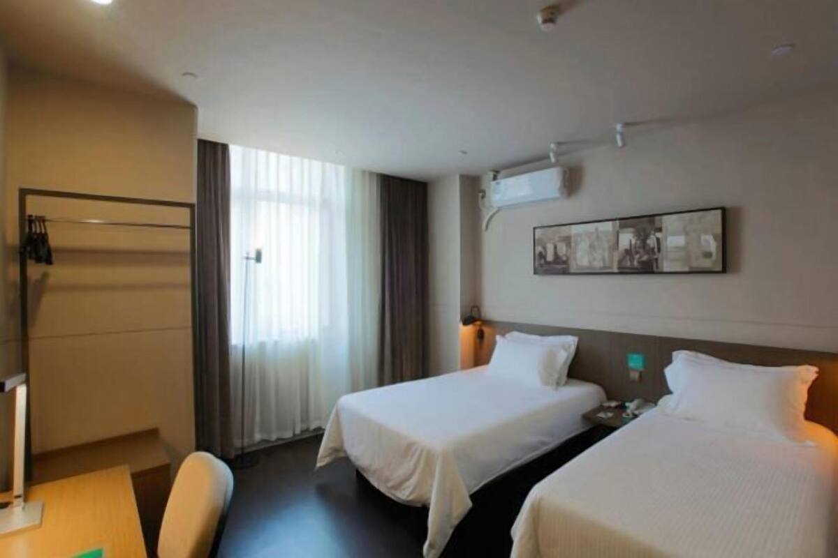 A hotel room with two beds, a desk, a chair, and a window with curtains.