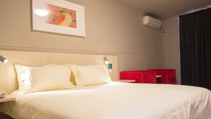 A hotel room with a large bed, a bedside table with a lamp, a red seating area, and an air conditioning unit on the wall. - Jinjiang Inn Select (Fanchang RT-Mart Business Square) (Wuhu)