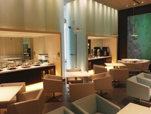 A modern dining area with multiple tables and chairs, a counter with kitchen appliances, and a green textured wall. - Jinjiang Inn Hongqiao National Exhibition Center (Shanghai)