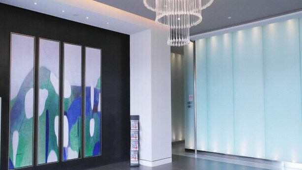 Um hall moderno com arte abstrata na parede, um lustre e um elevador de vidro.