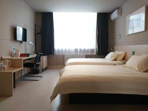 Ein Hotelzimmer mit zwei Betten, einem Schreibtisch, einem Sessel, einem Fernseher und einem Fenster mit Vorhängen.