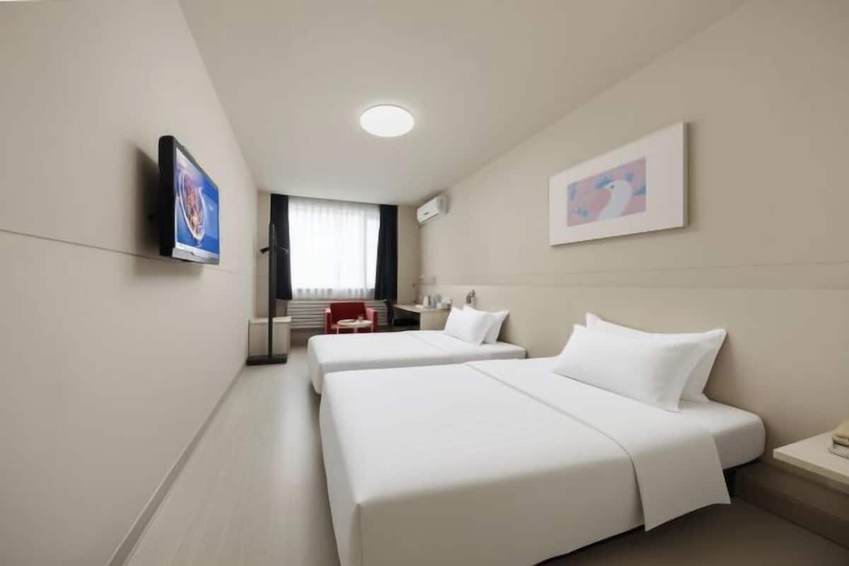 Ein Hotelzimmer mit zwei Betten, einem Fernseher, einem Schreibtisch und einem Fenster.