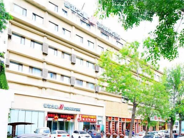 A multi-story hotel with a flat facade, multiple balconies, and a row of shops on the ground floor.