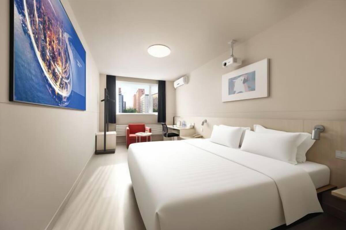 Ein Hotelzimmer mit einem großen Bett, einem Schreibtisch, einem Stuhl und einem Fenster mit Blick auf die Stadt.