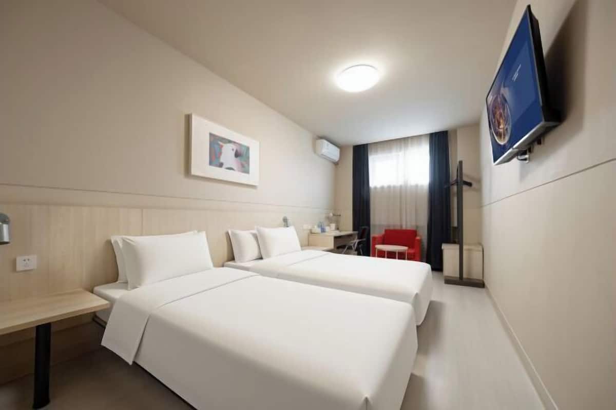 Ein Hotelzimmer mit zwei Betten, einem Schreibtisch, einem Stuhl, einem Fernseher und einem Fenster mit Vorhängen.