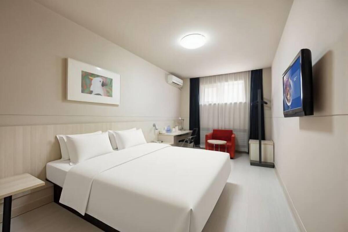 Ein Hotelzimmer mit Bett, Schreibtisch, Stuhl, Fernseher und einem Bild an der Wand.