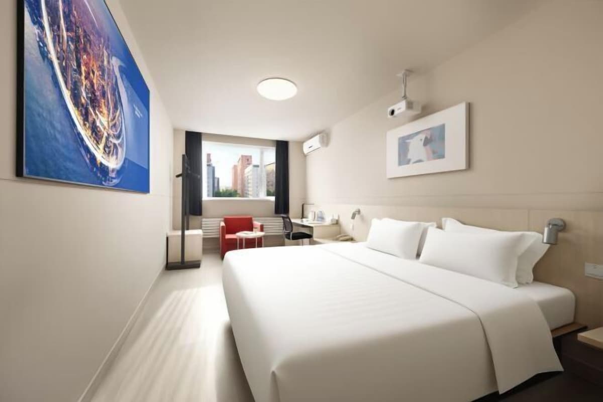 A hotel room with a large bed, a desk, a chair, and a window with a city view.
