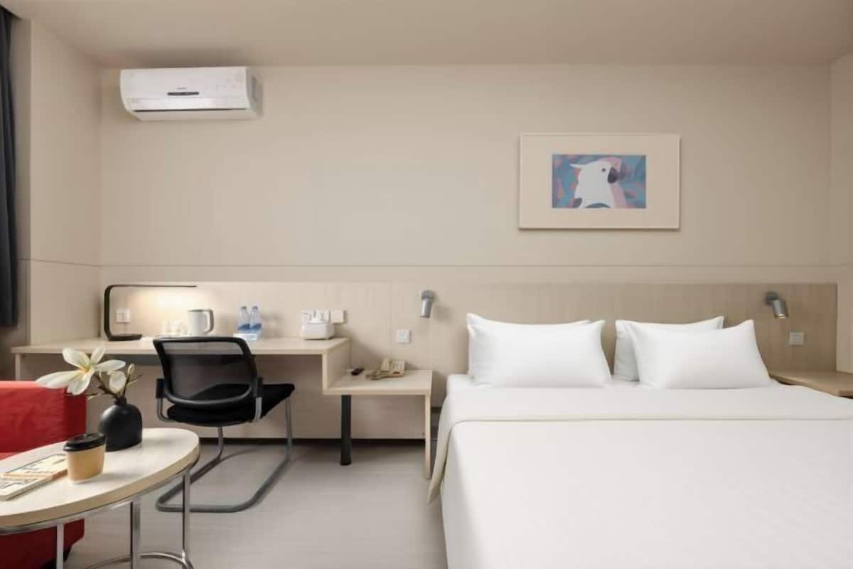 Ein Hotelzimmer mit Bett, Schreibtisch mit Stuhl, einem kleinen Tisch und einer Wand-Klimaanlage.