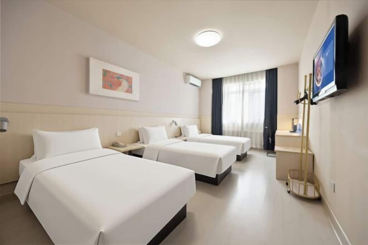 Ein Hotelzimmer mit drei Betten, einem Flachbildfernseher, einem Gemälde und einem Fenster mit Vorhängen.