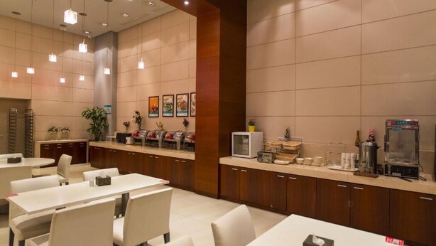 Un espace de restauration dans un hôtel, avec des tables et des chaises, un comptoir où sont disposés des distributeurs de nourriture et de boissons, et des œuvres d’art accrochées aux murs.