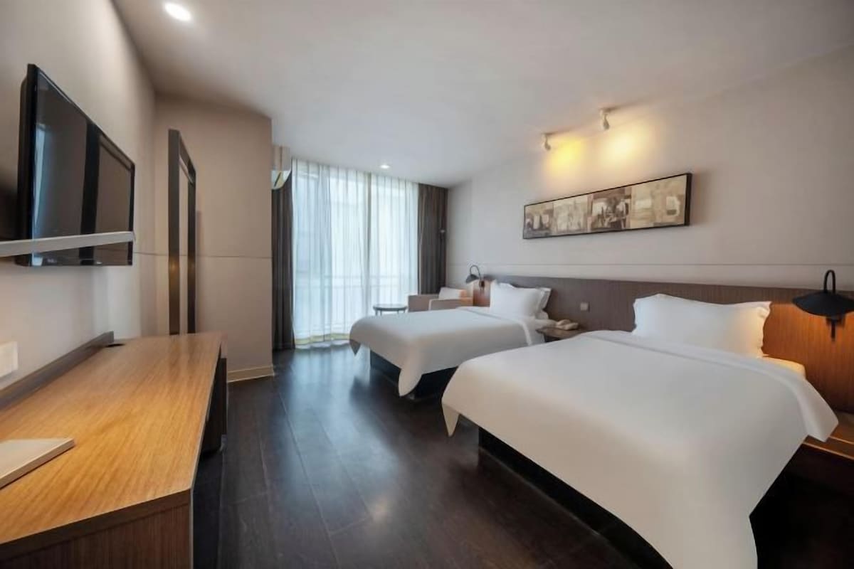 Une chambre d’hôtel avec deux lits, un bureau, une télévision et une grande fenêtre avec des rideaux.