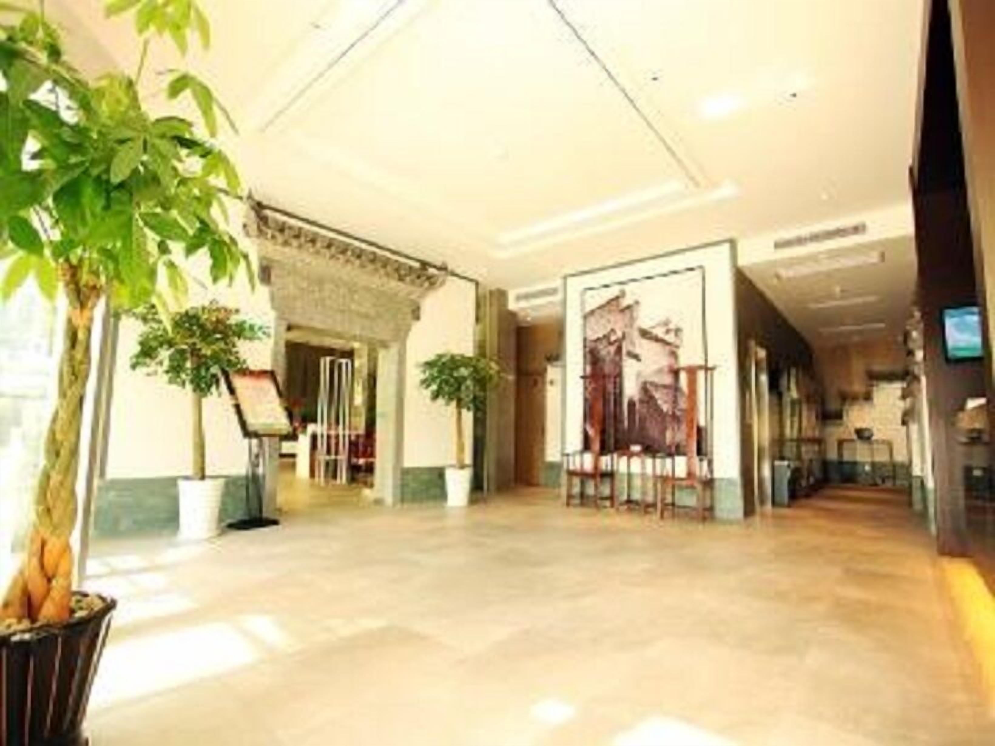 A hotel lobby with a tiled floor, potted plants, a reception desk, and a framed picture on the wall.