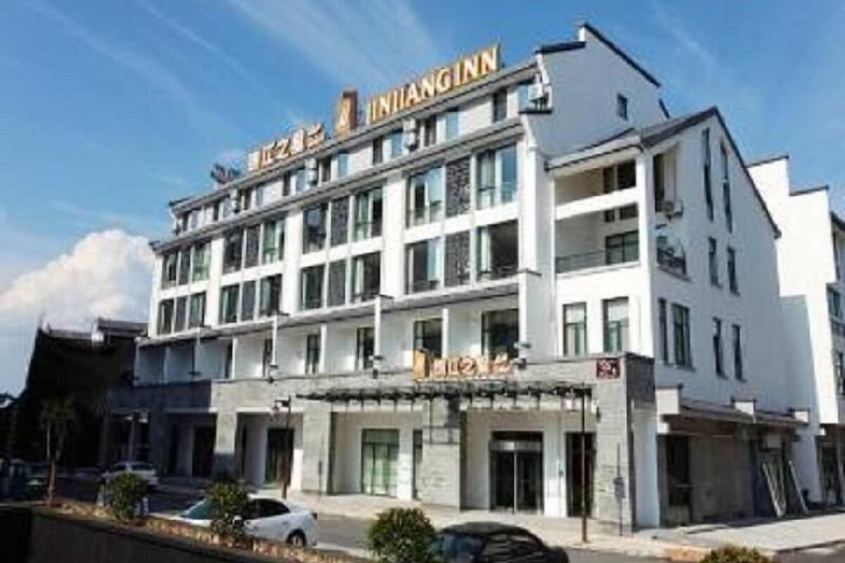 Hotel de vários andares com fachada chamativa, entrada no nível da rua e área de estacionamento visível.