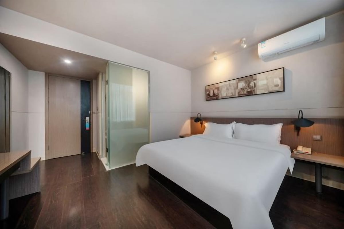 Une chambre d’hôtel moderne équipée d’un grand lit, d’un bureau, d’une chaise et d’une cloison en verre.