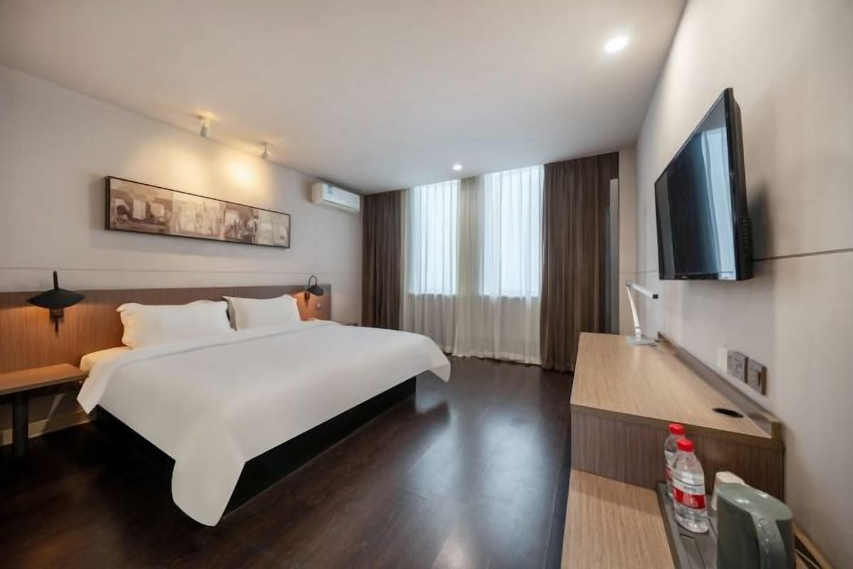Une chambre d’hôtel avec un grand lit, un bureau avec une chaise, un téléviseur à écran plat fixé au mur et une fenêtre avec des rideaux.