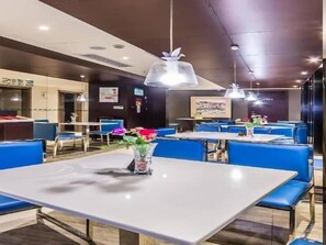 L’intérieur d’un restaurant avec des tables et des chaises bleues, des luminaires suspendus et un vase rempli de fleurs posé sur l’une des tables.