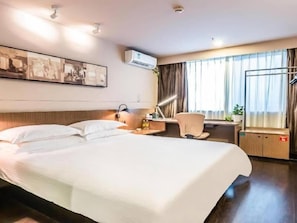 Quarto de hotel com cama grande, escrivaninha com cadeira, ar condicionado e janela com cortinas.
